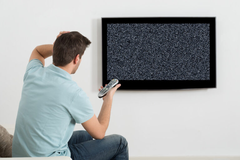 Homme assis sur un canapé devant la télévision sans signal